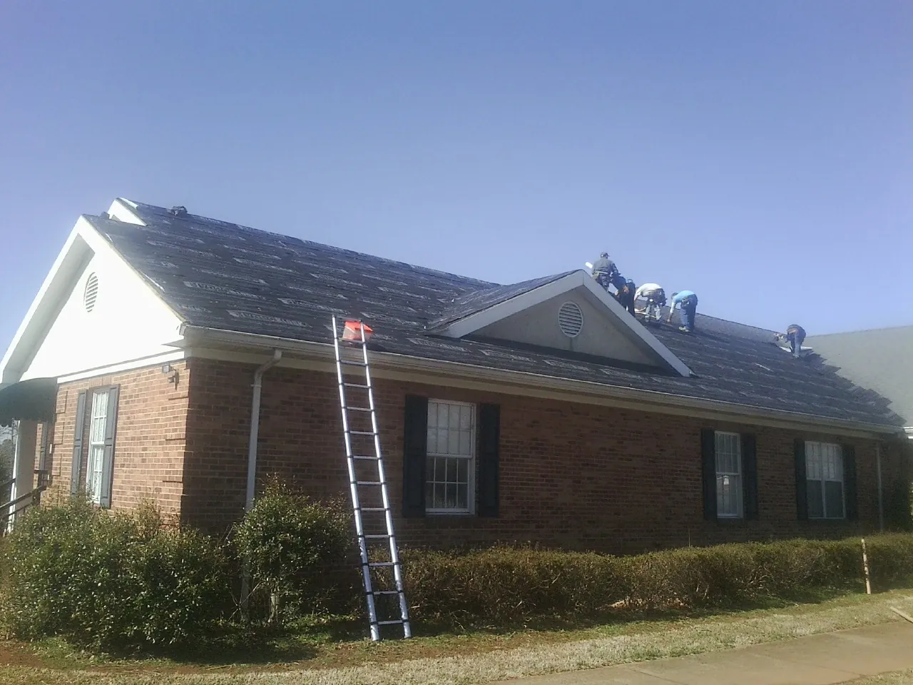 Crew tearing shingles off a brick ranch roof with a ladder set — Emergency Roof Repair work by our crew in Petrolia