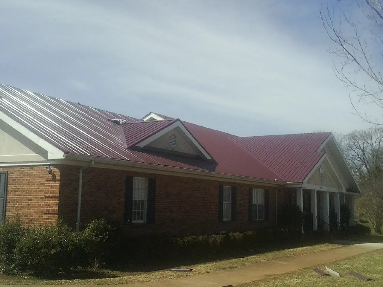 Red metal roof with gabled entries on a long brick building, from a Hail Damage Roof Repair job in Petrolia