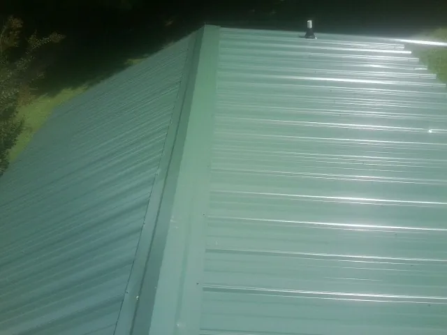 New green metal panels meeting at the ridge of a roof — Flat Roof Repair work by our crew in Petrolia