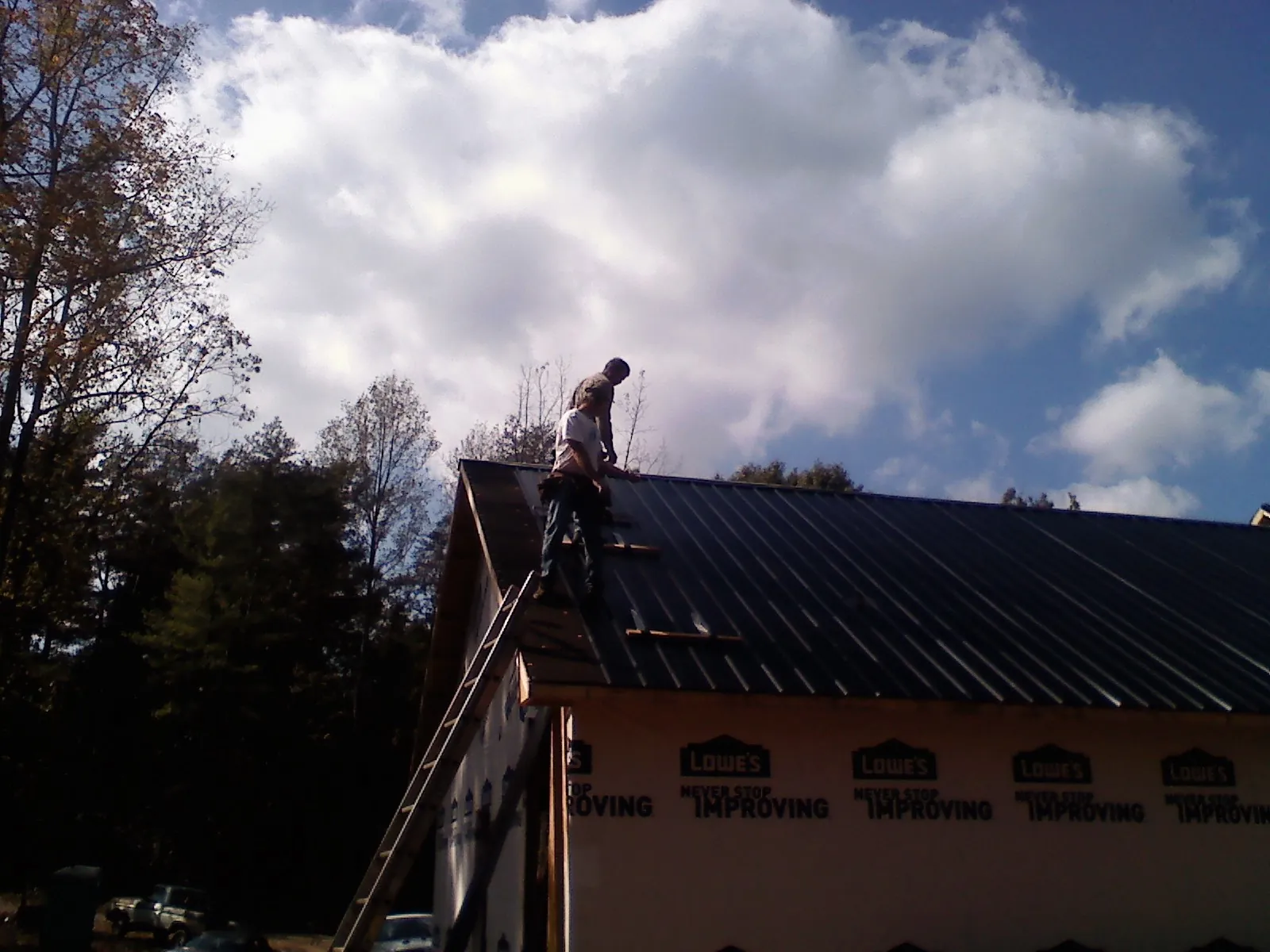 Roofer fastening dark metal panels high against a cloudy sky, from a Roof Inspection job in Petrolia