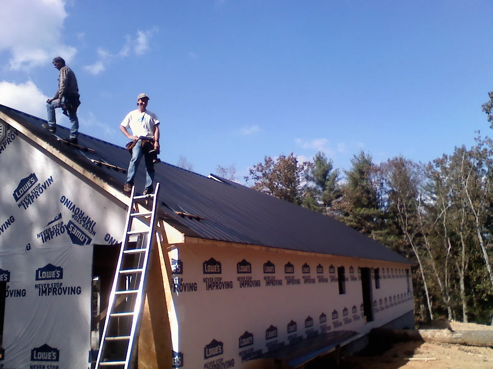 Two roofers standing on a long dark metal roof over a wrapped building in Petrolia