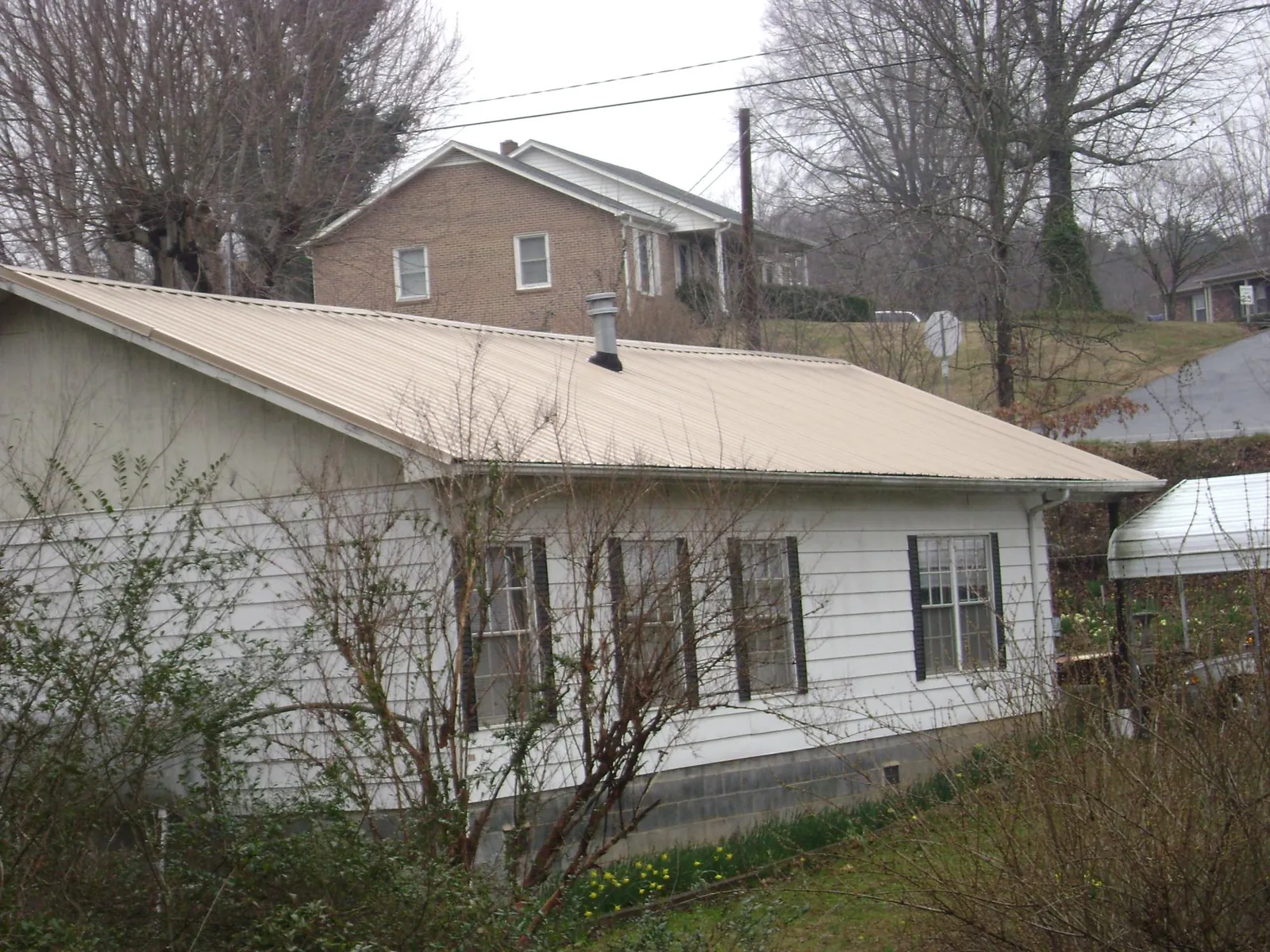 Tan metal roof on a white sided house set into a hillside — Commercial Roofing by Roofing Brothers in Petrolia