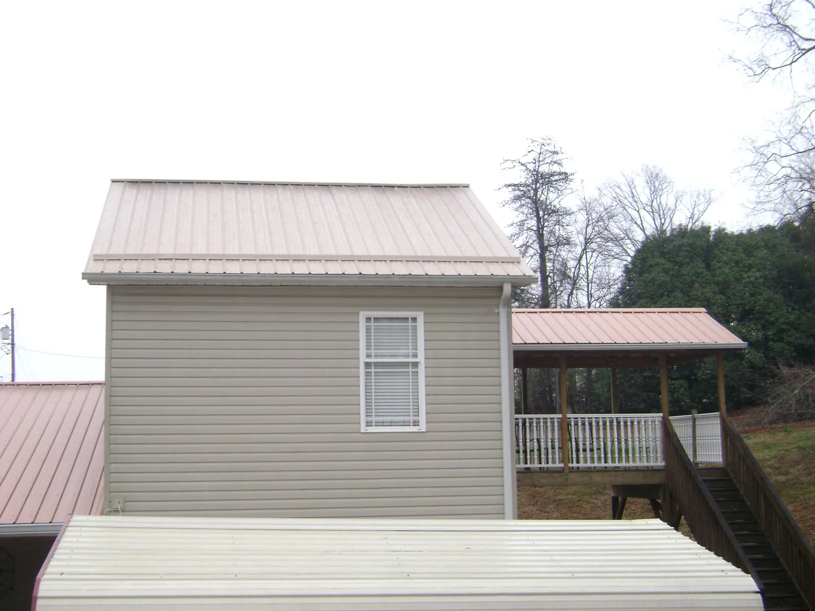 Tan metal roofs on a two story addition and attached porch, from a Roof Replacement job in Petrolia